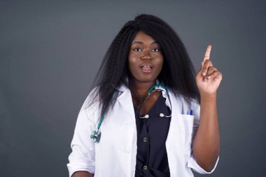 Çekici Afrikalı Amerikalı kadın doktorun yakın plan portresi bir parmağıyla yukarı bakıp gülümsüyor, bir fikrim var, cevabı ya da çözümü biliyorum..