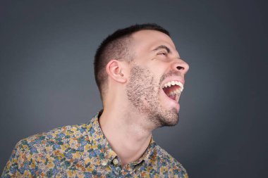 Neşeli Avrupalı bir adam iyi bir şakaya gülüyor ve eğleniyor ya da gri duvarda dikilerek günlük kıyafetler giyiyor. Mutlu adam içeride poz veriyor..