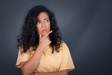 Tarz sahibi, genç esmer kadın portresi. Çenesinin altında elleri var ve yana bakıyor. Şüpheli ve şüpheci bir ifadeyle, endişe ve şüpheyle. Gri arka planda kapalı duruyor..