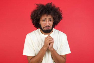 Afro saçlı genç adam kırmızı duvara karşı bir şey istiyor.   