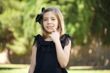  Kız kendine güvenen gülümsüyor çene hattına dokunuyor kameraya bakıyor başını yana eğmiş sırıtan beyaz dişlere seviniyor.