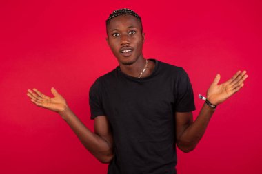 Ne olmuş yani? Kibirli, rahatsız edilmemiş, modern görünümlü, şık, siyah tişörtlü, kırmızı arka plan üzerine siyah tişörtlü, umursamaz, umursamaz, nefes nefese gülümseyen, bariz bir şey söyleyen Afrikalı Amerikalı adamın portresi..