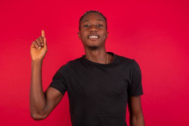 Genç Afro-Amerikan adam duvarın önünde duruyor ve parmaklarını bir numara ile gösteriyor ve gülümsüyor kendinden emin ve mutlu..