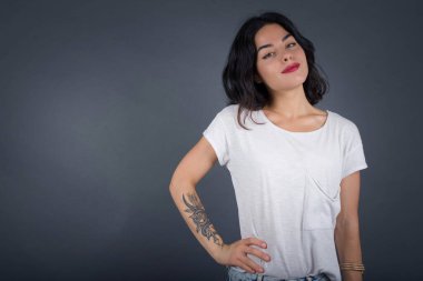 Neşeli bir kadının stüdyo çekimi elini kalçasında tutar, geniş bir gülümsemeyle, arkadaşlarının doğum gününde hazırladığı sürprizi bekler, gri arka planda izole bir şekilde.. 