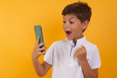 Sarı duvarda akıllı telefonu olan sevimli mutlu çocuk.  