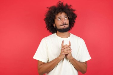 Afro saçlı genç adam kırmızı duvara karşı düşünüyor.   