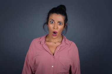Gri stüdyoda ağzı açık ve çenesi düşmüş afallamış genç bir kadın. 