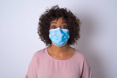 Yüz maskesi takan ve beyaz stüdyo arka planında izole edilmiş günlük kıyafetler giyen bir kadın.