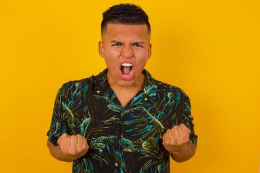 Güçlü, kararlı, gündelik giysiler içinde, kollarını sıkan, yumruklarını sıkan, golü neşe ve heyecanla haykıran Latin kökenli genç bir erkeğin portresi. Zafer, başarı ve başarı kavramı.