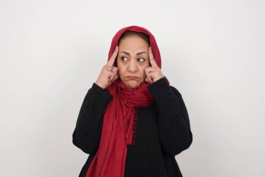 Hayalperest bir kadın, düşünceli bir ifadeyle, yüzünü yana çeviriyor, hoş bir şey düşünüyor, gri duvara karşı poz veriyor. Stüdyoda poz veren başörtüsü takan orta yaşlı bir Arap kadın.