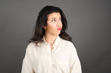 Güzel esmer kadın, sıradan giyinmiş, gri arka plana bakıyor..  