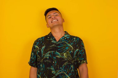 Gülümseyen, geniş gülümsemeli, beyaz dişli, sıradan tişörtlü, stüdyo duvarının başında duran yakışıklı İspanyol erkek izinli olduğu için seviniyor. İçerde dikilen adam.