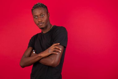 Kırmızı arka plan girişimcisi üzerinde siyah tişört giyen yakışıklı, kendine güvenen, neşeli, Afro-Amerikan bir adamın belden yukarısında geniş bir gülümsemesi, kolları çapraz kolları var, şık giyinmiş, iş arkadaşıyla tanıştığına memnun olmuş..