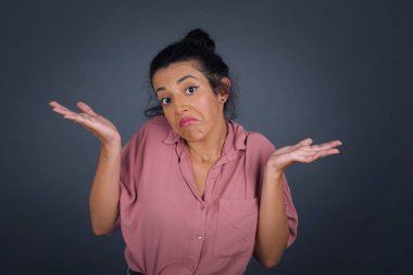 Kafası karışmış, kolları açık genç bir kadın omuzlarını silkip 