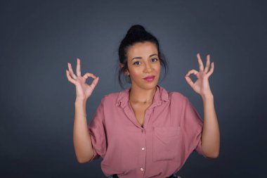 Çekici bir kadının iki eliyle işaret dili göstermesine sevindim. Onayladığına, neşeli bir ifadesi olduğuna sevindim. Gri duvara yaslanarak.