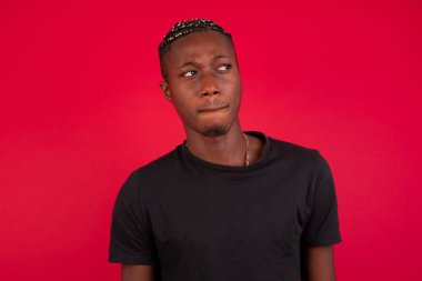 Şaşırmış genç Afrikalı Amerikalı adamın fotoğrafı dudaklarını kıvırıyor ve endişeli bir bakış atıyor, önünde korkunç bir şey görüyor, beyaz arka planda izole edilmiş, kot pantolon giymiş..