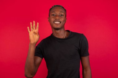 Duvara yaslanmış genç bir adam dört numarayı gösterip işaret ederken kendinden emin ve mutlu gülümsüyor..