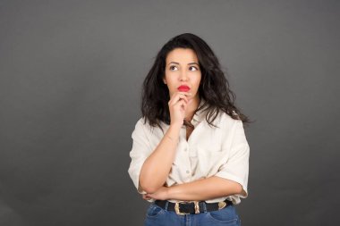 Güzel esmer kadın, sıradan giyinmiş, düşünceli. Gri arkaplanda duruyor.  
