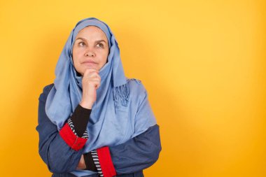 Düşünceli orta yaşlı tesettürlü Müslüman kadın portresi elini çenesinin altında tutuyor, yana bakıyor, stüdyoya karşı ilgi duyan bir şey düşünüyor ya da merak ediyor. Karar alma kavramı.