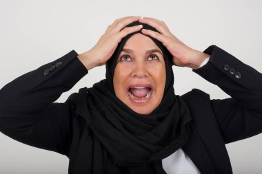 Korkunç, stres, şok. Siyah tesettürlü genç, duygusal, çılgın Müslüman bir kadının portresi el ele tutuşuyor. İnsani duygular, yüz ifadesi kavramı. Moda renkleri. Ön görünüm