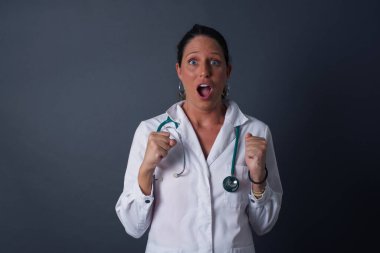 İnsan yüzü ifadeleri ve duyguları. Gri arka planda izole edilmiş genç doktor portresi paniğe kapılmış görünüyor, ellerini yüzüne yakın tutuyor, ağzı sonuna kadar açık. Sürpriz ve şok..