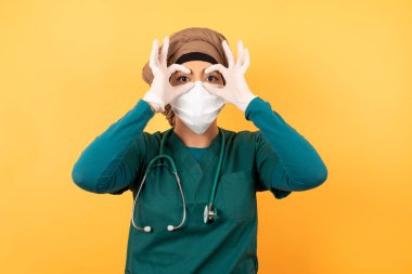 Neşeli, genç, güzel, yeşil üniformalı, Müslüman bir doktor iki eliyle Ok hareketlerini gösteriyor, gözlük takıyormuş gibi yapıyor, şaşırtıcı bir şey gördüğüne şaşırıyor. Duygular, vücut dili ve jestler.