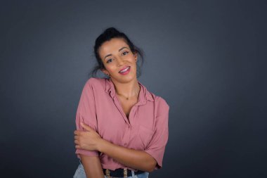 Gri stüdyo arka planında poz veren utangaç esmer kadın.