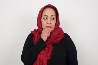 Düşünceli, olgun Müslüman bir kadın eli çenesinin altında, düşünceli bir şekilde yukarı bakıyor.