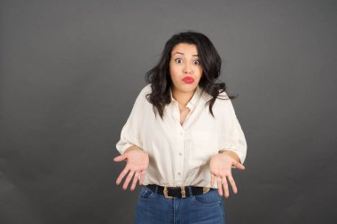 Güzel esmer kadının kafası karışmış. Gri arkaplanda duruyor. 