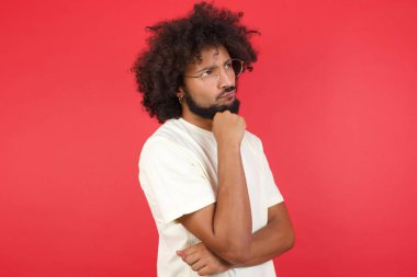 Kızıl duvara karşı düşünen afro saçlı genç bir adam.   