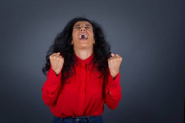 Kıvırcık saçlı, kırmızı tişörtlü güzel esmer kadının portresi heyecanla bakıyor, ellerini havada tutuyor, beklenmedik bir şey fark ediyor, dışarıda poz veriyor. Güzel bir kadın ani haberlere tepki verir.