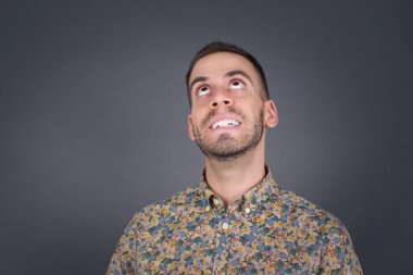 Esrarengiz bir gülümsemeyle yukarı bakan düz saçlı gizemli erkek portresi. Yakışıklı, gülümseyen çocuk gri duvara bakıyor..