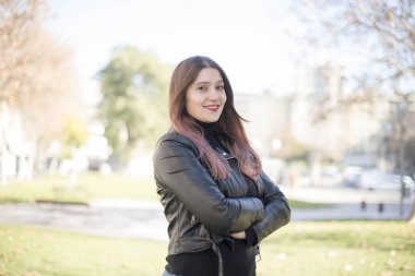 Parkta kollarını kavuşturmuş genç ve güzel bir kadın.