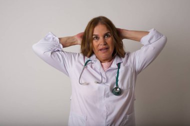 Güven ve cinsel ilişki konsepti. Çekici beyaz kadın doktor portresi, kendinden emin bir ifadeyle gülümseyen ve ellerini başının üstünde tutan. Gri arkaplanda duruyor.