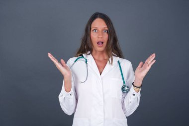 Sürpriz konsept. Şaşırmış güzel doktor kızın portresi. İnanamamasına şaşırmış gibi görünüyor. Ağzın açık, yüzün yanında ellerin var. Olumlu duygu yüz ifadesi vücut dili.