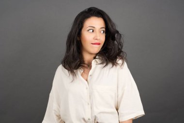 Güzel esmer kadın, sıradan giyinmiş, gri arka plana bakıyor..  