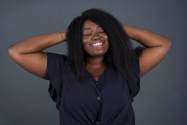 Güven ve cinsel ilişki konsepti. Çekici, Afro-Amerikalı bir kadının portresi. Kendine güvenen bir ifadeyle gülümseyen ve ellerini başının üstüne koyan bir kadın. Gri arkaplanda duruyor. 