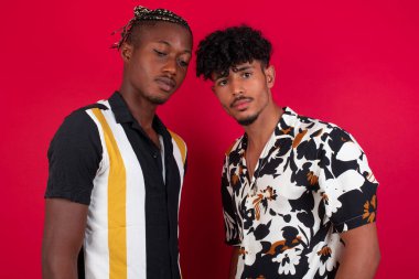 Bir grup genç, çok ırklı çekici arkadaş şık damalı tişörtler giyiyor, birlikte gülüyor ve eğleniyorlar, kırmızı stüdyo arka planında poz veriyorlar. 