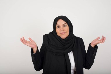 Kafası karışmış, siyah tesettürlü, kolları açık, omuzlarını silkip 