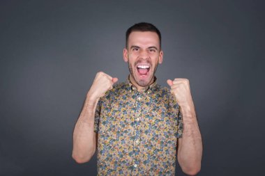 Kafkasyalı genç adam başarısını ve zaferini kutluyor yumruklarını neşeyle sıkıyor. Hedefine ve amaçlarına ulaşmaktan mutlu olan şapkalı şanslı adam. Pozitif duygular, duygular..