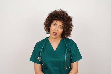 Etkileyici yüz ifadeleri. Şok olmuş güzel Arap doktor kadın tıbbi üniforma giyiyor, gördüklerinden şaşkına dönüyor. 