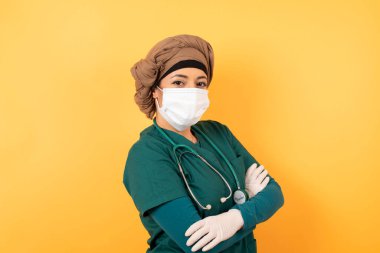 Yüzünde maske olan neşeli bir Arap kadın hayal et. Kapalı yerde kollarını kavuşturmuş duruyor. Kameraya bakıp gülümsüyor.. 