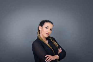 Gri duvara yaslanmış, kolları çaprazlanmış, gündelik giysiler giymiş beyaz bir kadın. Kameraya bakıp gülümsüyor. Kendine güvenen başarılı bir kadın..