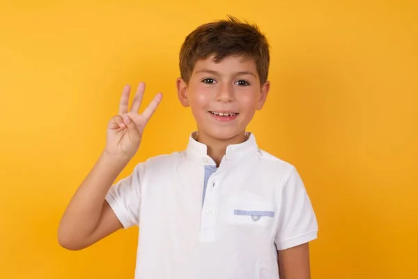 黄色の壁に3本の指を示すかわいい男の子 — ストック写真