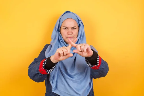 壁に向かって立っている孤立した背景の上にヒジャブにいる中年のイスラム教徒の女性 否定的なサインをしている指を交差する怒りの表現を拒否しています — ストック写真
