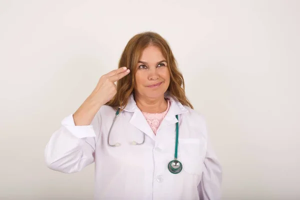 Unhappy Mature Caucasian Doctor Woman Wearing Medical Uniform Imitates Gun — Stock Photo, Image