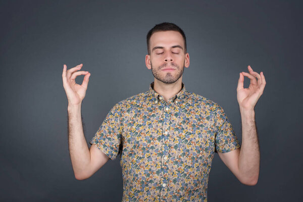 Красивый молодой человек, занимающийся йогой утром в помещении после пробуждения, закрывая глаза, держа пальцы в жесте мудры. 