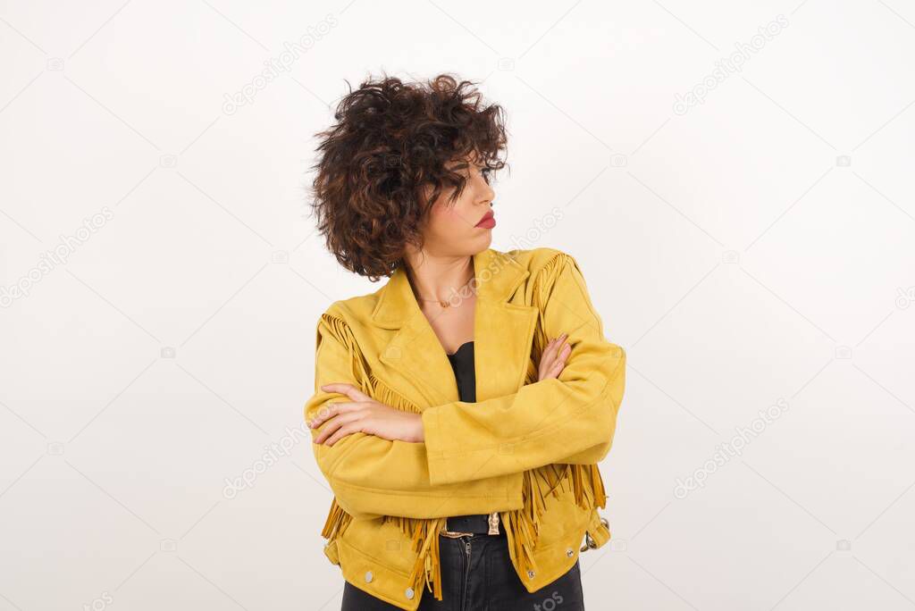 Image of upset pretty young  lady standing indoors with arms crossed. Looking with disappointed expression aside after listening to bad news. Confident girl.