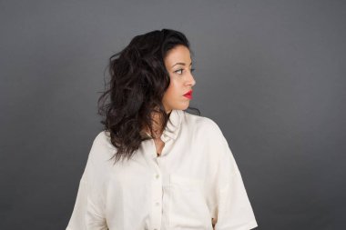 Güzel esmer kadın, sıradan giyinmiş, gri arka plana bakıyor..  