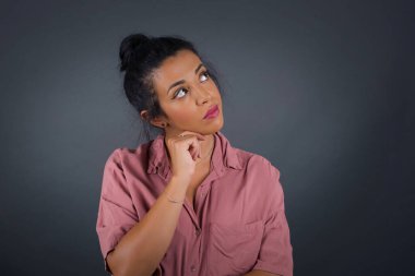 Düşünceli genç bir kadın, arkadaşının doğum günü partisinde ne giyeceğine karar veremezken elini başının altında tutuyor, şüpheli bakışlar atıyor. 